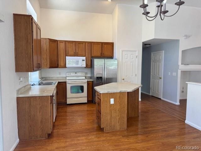 20148 E Dartmouth Dr, Aurora, CO 80013 - kitchen featuring white appliances, a towering ceiling, a sink, a kitchen island, and brown cabinetry