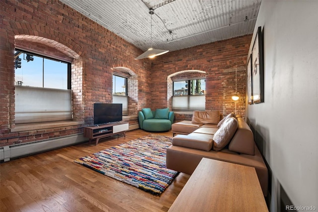 living room featuring hardwood / wood-style floors, a high ceiling, brick wall, and a baseboard heating unit