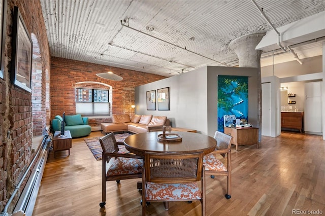 dining room featuring a baseboard heating unit, hardwood / wood-style floors, and brick wall