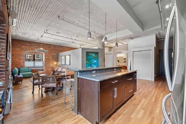 kitchen with brick wall, decorative light fixtures, light hardwood / wood-style flooring, a center island, and stainless steel fridge