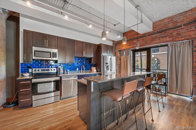 kitchen with stainless steel appliances, a kitchen island, light wood-type flooring, decorative light fixtures, and dark stone countertops