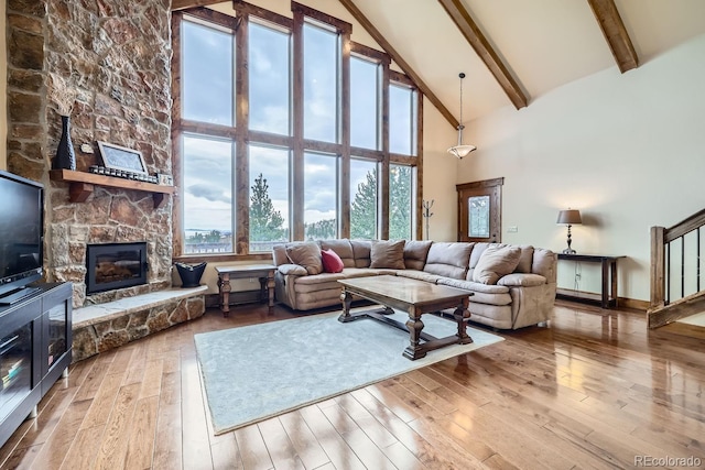 living room with high vaulted ceiling, light wood-type flooring, beamed ceiling, and a stone fireplace