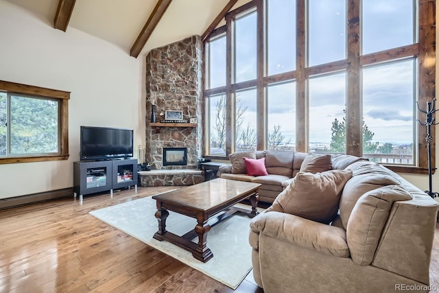 living room featuring baseboard heating, a fireplace, light wood-type flooring, high vaulted ceiling, and beam ceiling