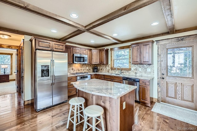 kitchen with a breakfast bar area, stainless steel appliances, a center island, light stone counters, and sink