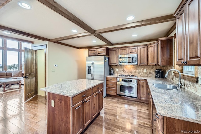 kitchen featuring appliances with stainless steel finishes, sink, light stone counters, and a kitchen island