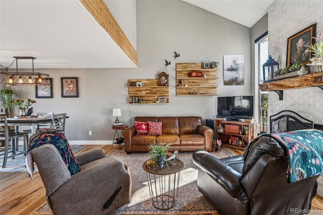 living area with lofted ceiling, a fireplace, baseboards, and wood finished floors