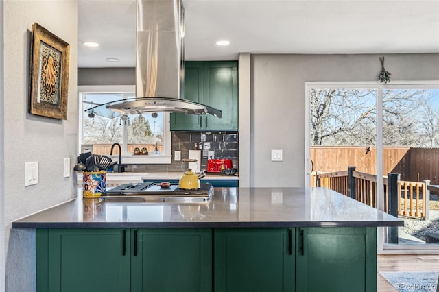 kitchen featuring island range hood, decorative backsplash, wood finished floors, stainless steel gas cooktop, and green cabinetry