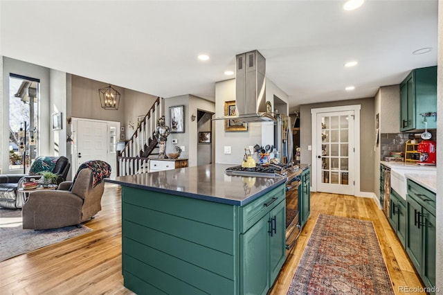 kitchen with green cabinets, light wood-type flooring, tasteful backsplash, island exhaust hood, and gas range