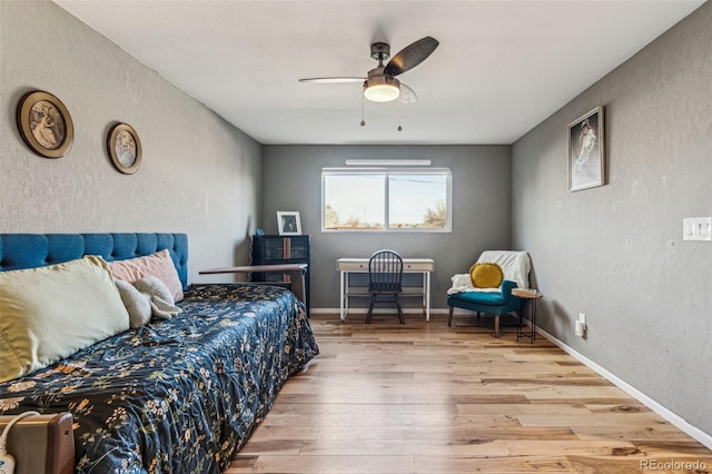 bedroom featuring a ceiling fan, baseboards, wood finished floors, and a textured wall