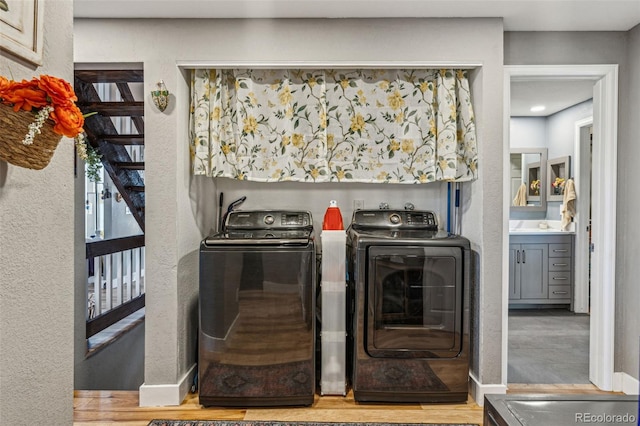 clothes washing area featuring a textured wall, wood finished floors, laundry area, independent washer and dryer, and baseboards