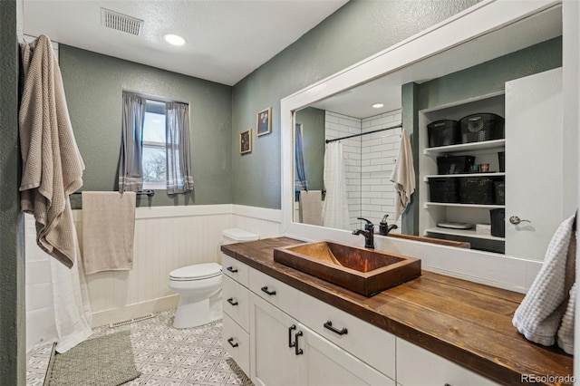 bathroom with toilet, a shower with shower curtain, vanity, visible vents, and wainscoting