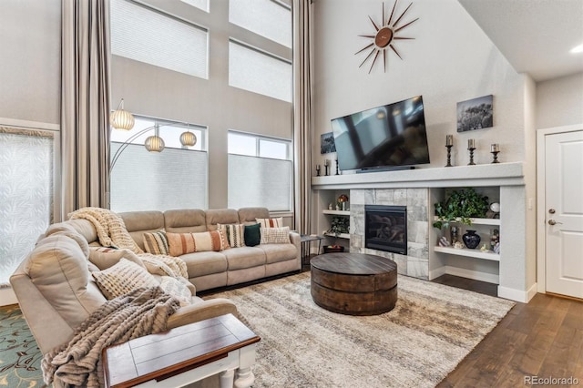 living area featuring a tiled fireplace, a high ceiling, baseboards, and wood finished floors