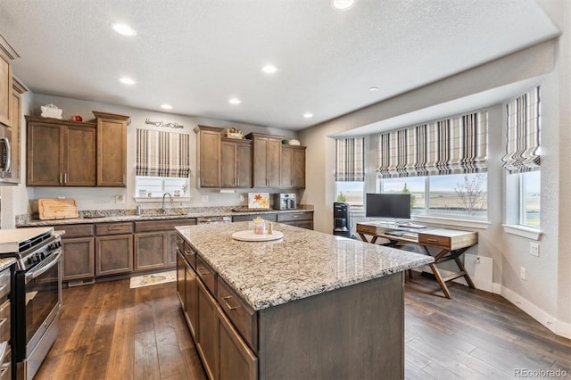 kitchen with dark wood-style floors, a kitchen island, light stone countertops, appliances with stainless steel finishes, and a sink