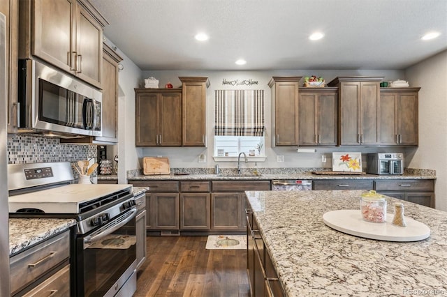 kitchen featuring dark wood-type flooring, appliances with stainless steel finishes, light stone counters, a sink, and backsplash
