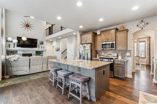 kitchen featuring dark wood finished floors, a kitchen bar, arched walkways, a kitchen island, and appliances with stainless steel finishes