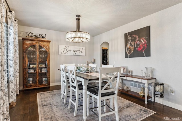 dining area with arched walkways, baseboards, a textured ceiling, and wood finished floors