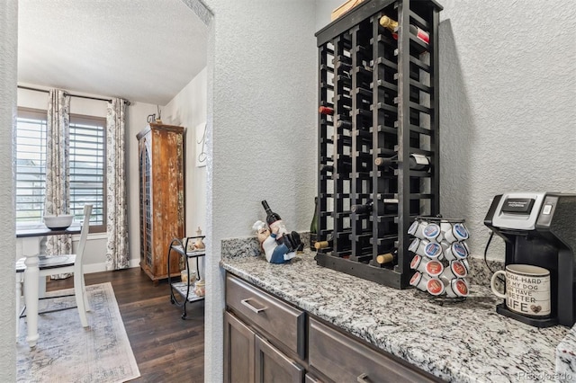 wine area featuring a textured wall, a textured ceiling, and dark wood finished floors