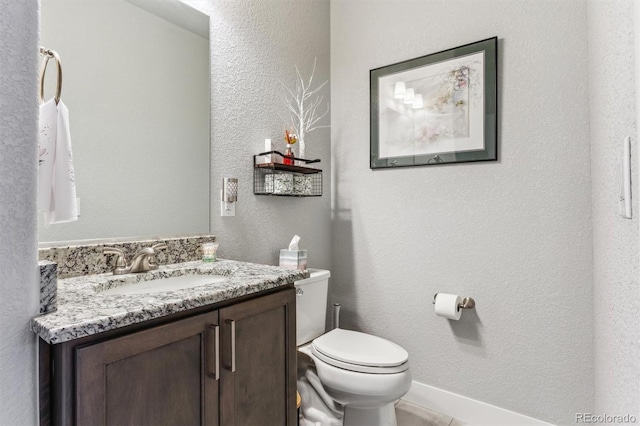 half bathroom with a textured wall, vanity, and toilet