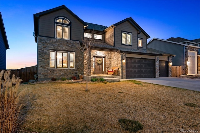 traditional-style house featuring driveway, fence, stone siding, and a front yard