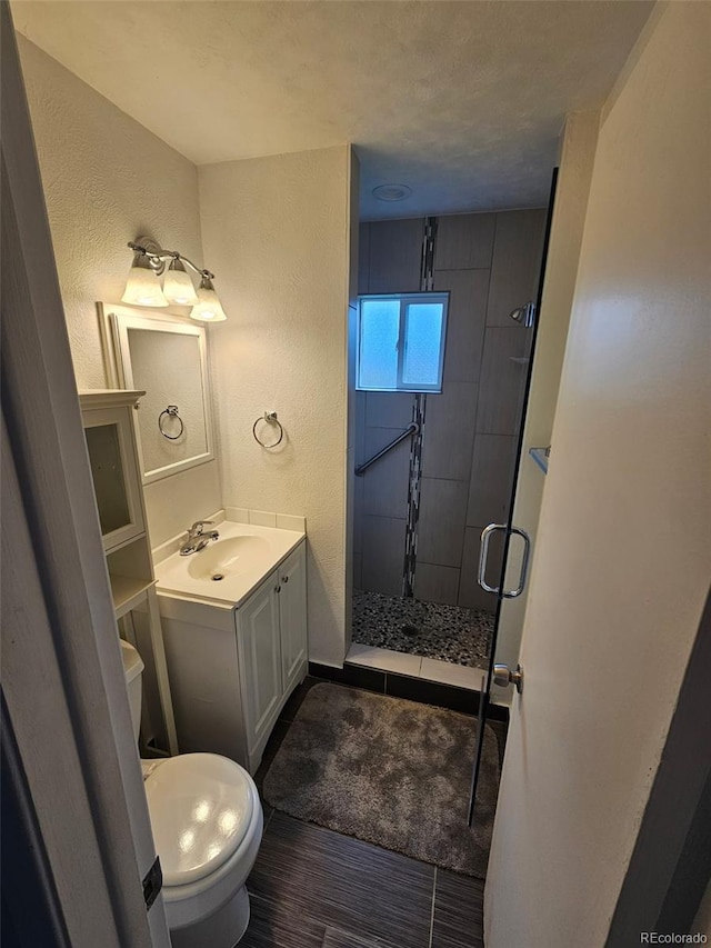 3905 Nelson St, Wheat Ridge, CO 80033 - bathroom with a stall shower, a textured wall, vanity, toilet, and wood finished floors