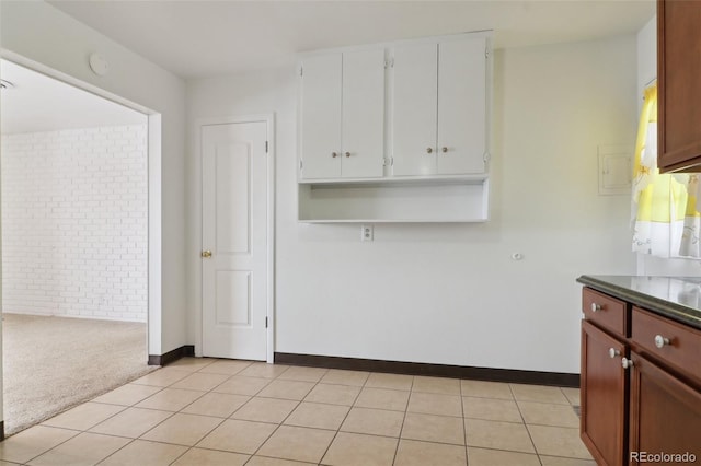 kitchen featuring brick wall, light carpet, and white cabinets