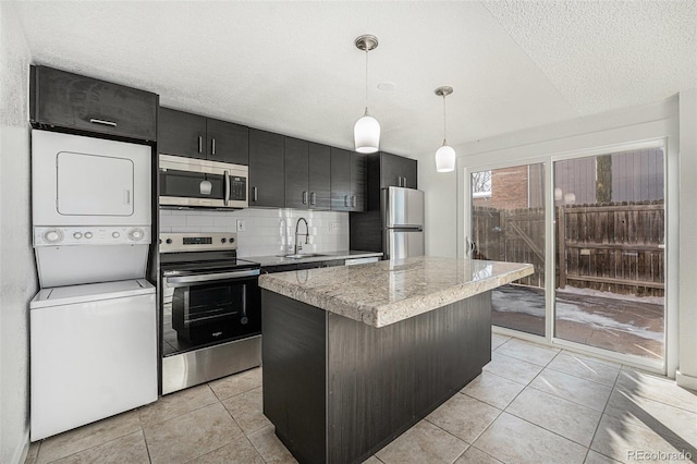 kitchen with a kitchen island, sink, hanging light fixtures, stacked washer / drying machine, and stainless steel appliances