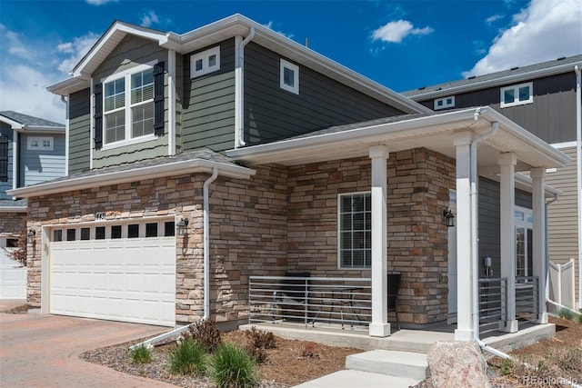 view of front of house with stone siding, an attached garage, covered porch, and driveway