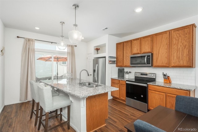 kitchen featuring stainless steel appliances, a sink, backsplash, dark wood-style floors, and a kitchen island with sink