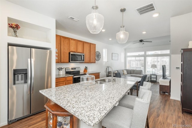 kitchen with appliances with stainless steel finishes, a sink, brown cabinets, a kitchen bar, and recessed lighting