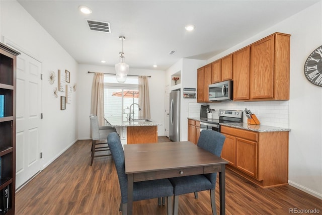 kitchen with stainless steel appliances, dark wood-style floors, decorative backsplash, an island with sink, and a sink
