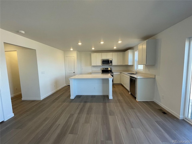 kitchen with stainless steel appliances, visible vents, baseboards, a center island, and dark wood finished floors