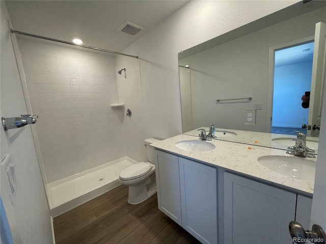 full bath with visible vents, a sink, a tile shower, and wood finished floors