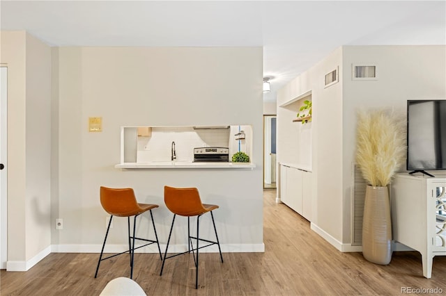 kitchen with electric range, light hardwood / wood-style flooring, a kitchen breakfast bar, and kitchen peninsula