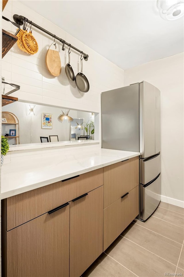 kitchen featuring stainless steel refrigerator, light tile patterned flooring, light stone counters, and light brown cabinets