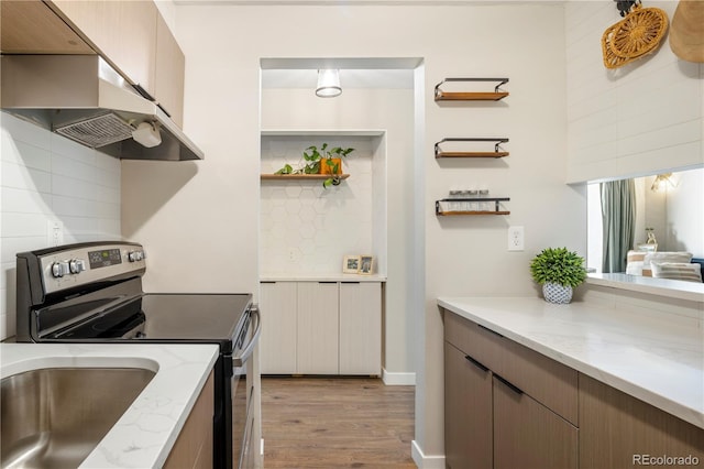 kitchen featuring stainless steel electric range oven, light wood-type flooring, backsplash, and light stone counters