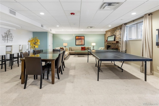 game room with a stone fireplace, a paneled ceiling, and light colored carpet