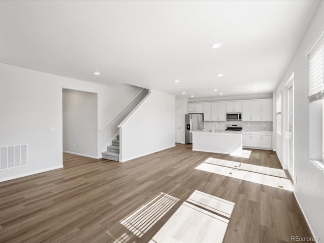 8850 Sedalia St, Commerce City, CO 80022 - unfurnished living room with light wood-style floors, recessed lighting, stairs, baseboards, and a sink