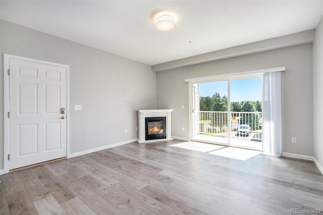 unfurnished living room featuring a glass covered fireplace, baseboards, and wood finished floors