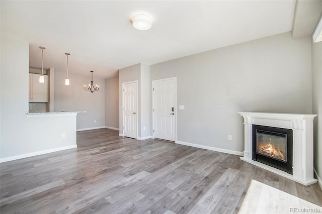 unfurnished living room featuring a glass covered fireplace, wood finished floors, baseboards, and a chandelier