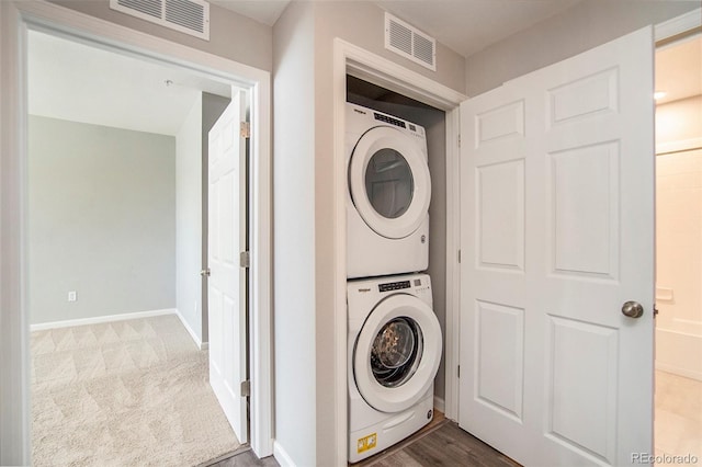 laundry area featuring visible vents, baseboards, stacked washer and clothes dryer, and carpet flooring