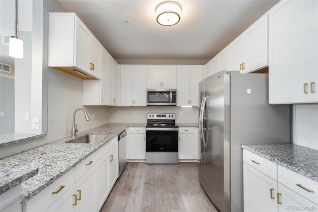 kitchen with light stone counters, a sink, stainless steel appliances, white cabinets, and light wood-type flooring