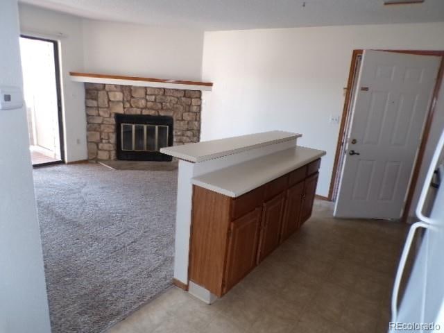 kitchen with a stone fireplace, light colored carpet, and kitchen peninsula