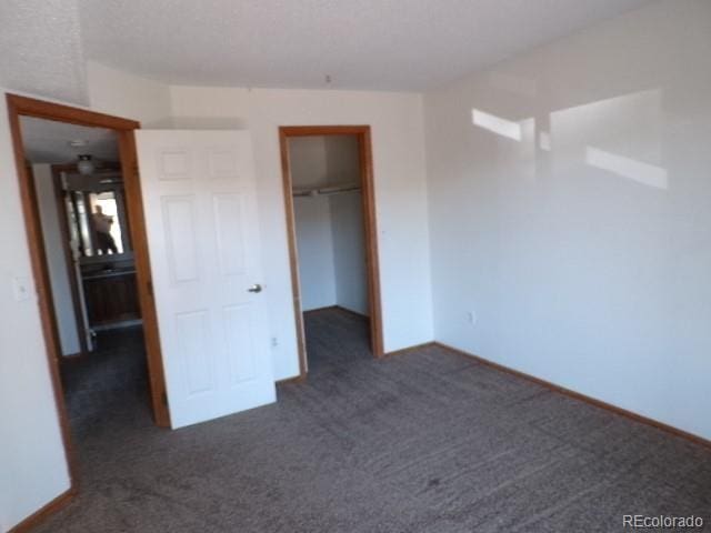 unfurnished bedroom with dark colored carpet, a walk in closet, and a closet