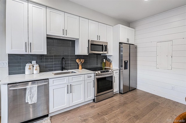 kitchen featuring appliances with stainless steel finishes, a sink, tasteful backsplash, white cabinetry, and light wood-style floors