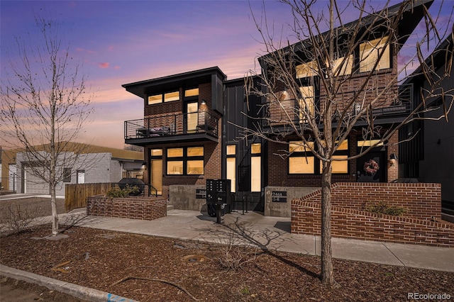 back of property at dusk with a balcony and brick siding