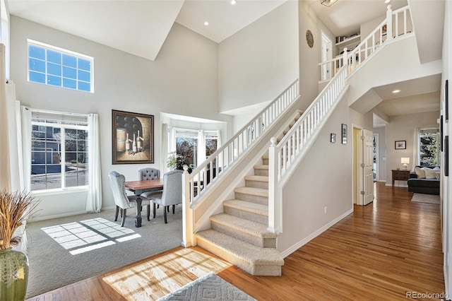 stairway with recessed lighting, wood finished floors, a towering ceiling, and baseboards