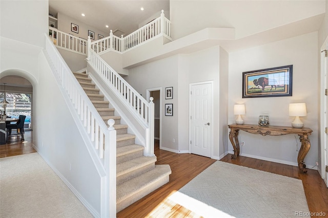 stairs with arched walkways, wood finished floors, a towering ceiling, and baseboards