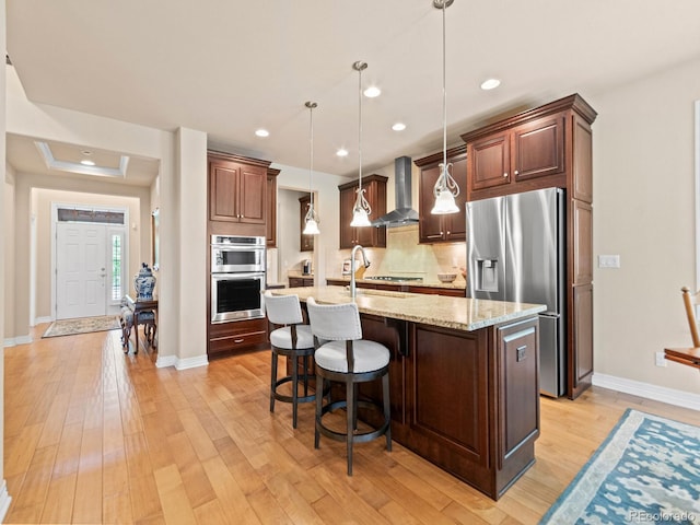 13645 Osage Ct, Broomfield, CO 80023 - kitchen with stainless steel appliances, wall chimney range hood, light wood finished floors, a center island with sink, and backsplash