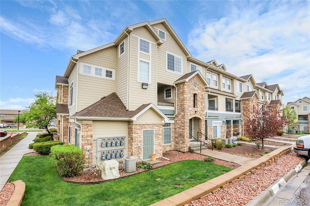 multi unit property with stone siding, a residential view, a front yard, and roof with shingles