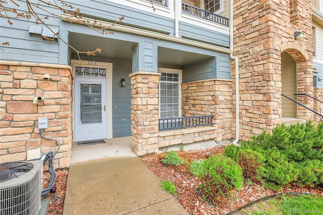 property entrance with central AC unit, a balcony, brick siding, and covered porch